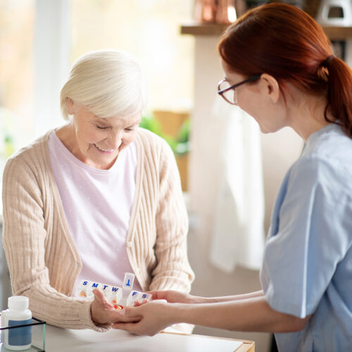 Pensioner taking vitamins standing near caregiver