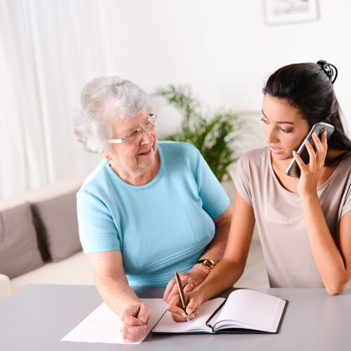 cheerful young woman helping old person doing paperwork and telephone call