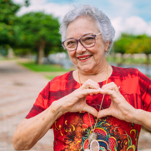 Joyful senior lady in glasses laughing heart with hands. Latin A